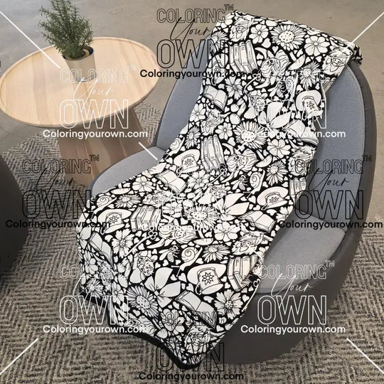 Black and white uncolored highland cow with books and tea patterned blanket with a black fleece lined underside draped over a gray chair.