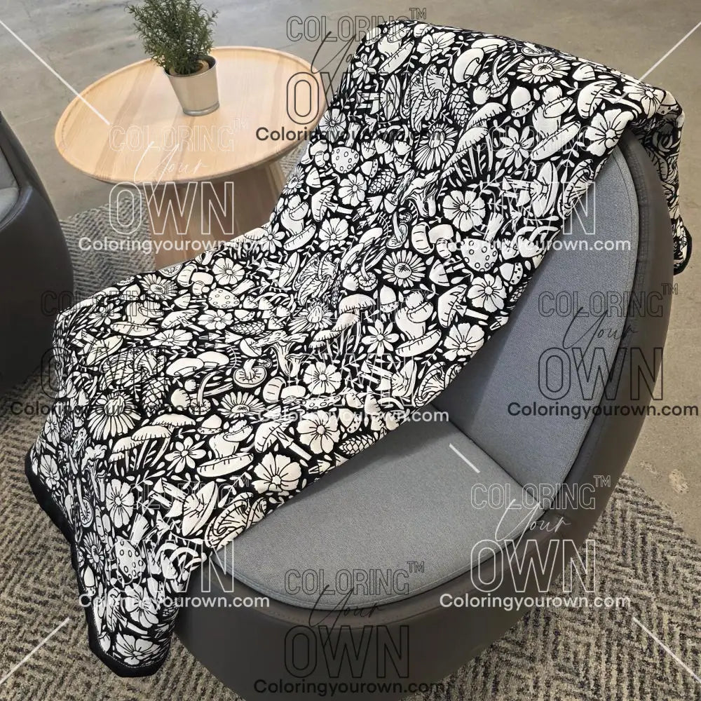 Black and white uncolored mushroom and floral patterned blanket with black fleece lined underside draped over a gray chair.