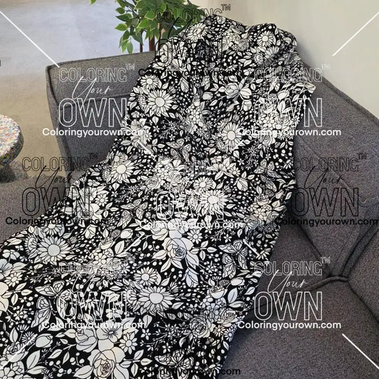 Black and white uncolored vintage floral and butterfly patterned blanket with a black fleece lined underside draped over a gray couch.