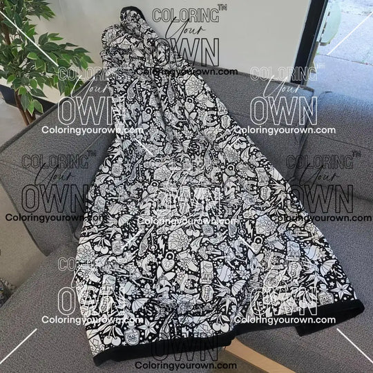 Black and white uncolored classic tattoo styles and patterns blanket with a black fleece lined underside draped over a gray couch.