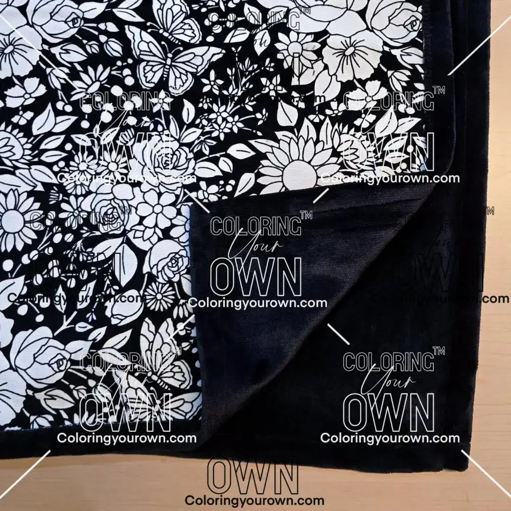 Black and white uncolored vintage floral and butterfly patterned blanket with close up view showing black fleece lined underside