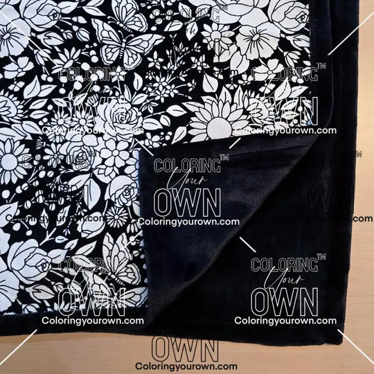 Black and white uncolored vintage floral and butterfly patterned blanket with close up view showing black fleece lined underside