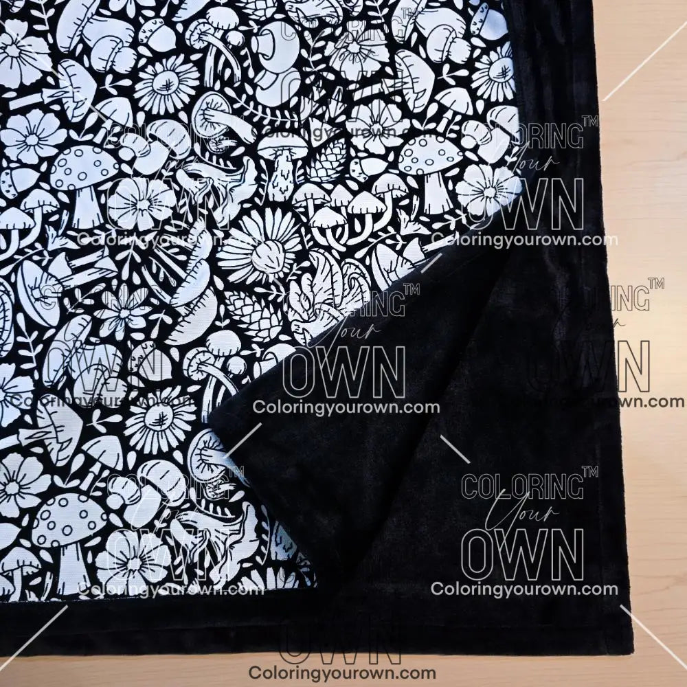 Black and white uncolored mushroom and floral patterned blanket with close up view showing black fleece lined underside