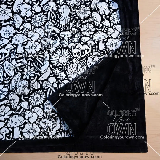 Black and white uncolored mushroom and floral patterned blanket with close up view showing black fleece lined underside