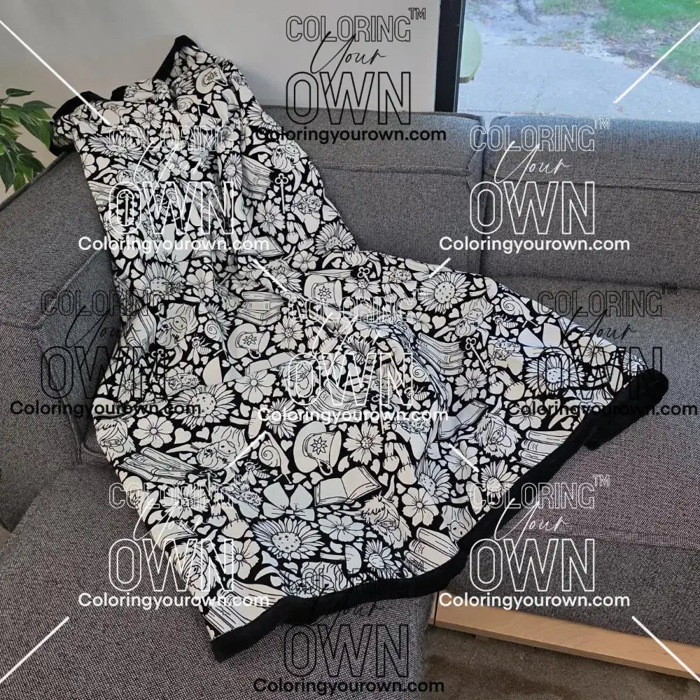 Black and white uncolored highland cow with books and tea patterned blanket with a black fleece lined underside draped over a gray couch.