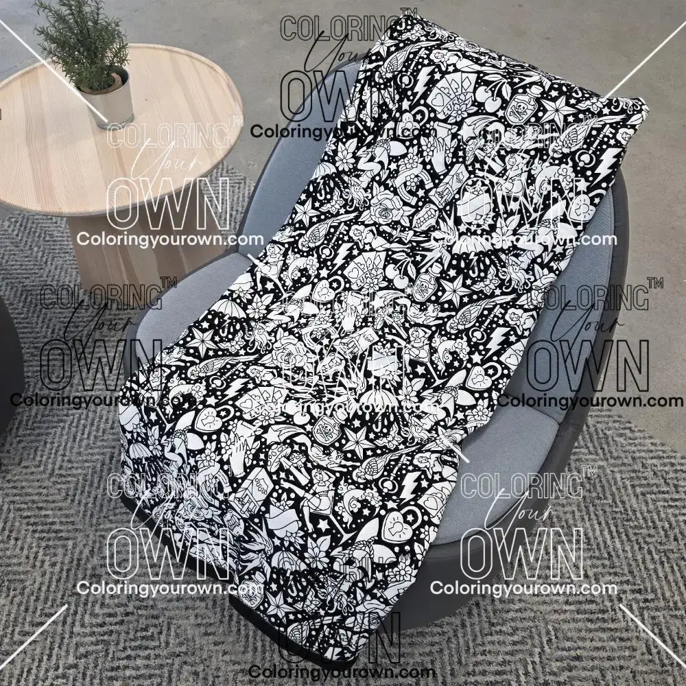 Black and white uncolored classic tattoo styles and patterns blanket with a black fleece lined underside draped over a gray chair.