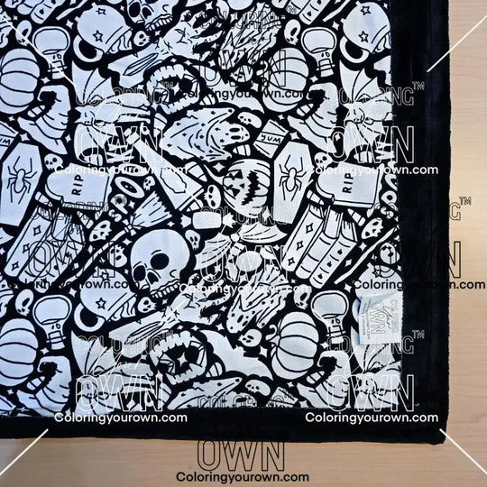 Black and white uncolored spooky Halloween patterned blanket with skulls, ghosts and pumpkins with black fleece lined underside close up view