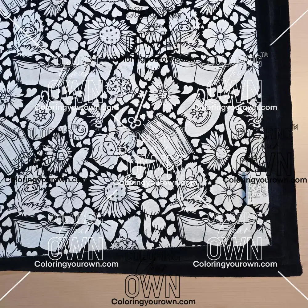 Black and white uncolored highland cow with books and tea  patterned blanket with black fleece lined underside close up view