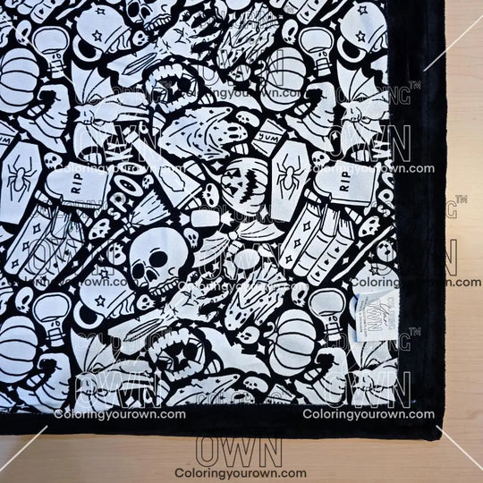 Black and white uncolored spooky Halloween patterned blanket with skulls, ghosts and pumpkins with black fleece lined underside close up view