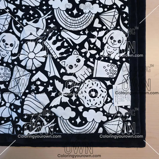 Black and white uncolored version two doodle patterned blanket with donuts, cats, cupcakes  patterned blanket with black fleece lined underside close up view