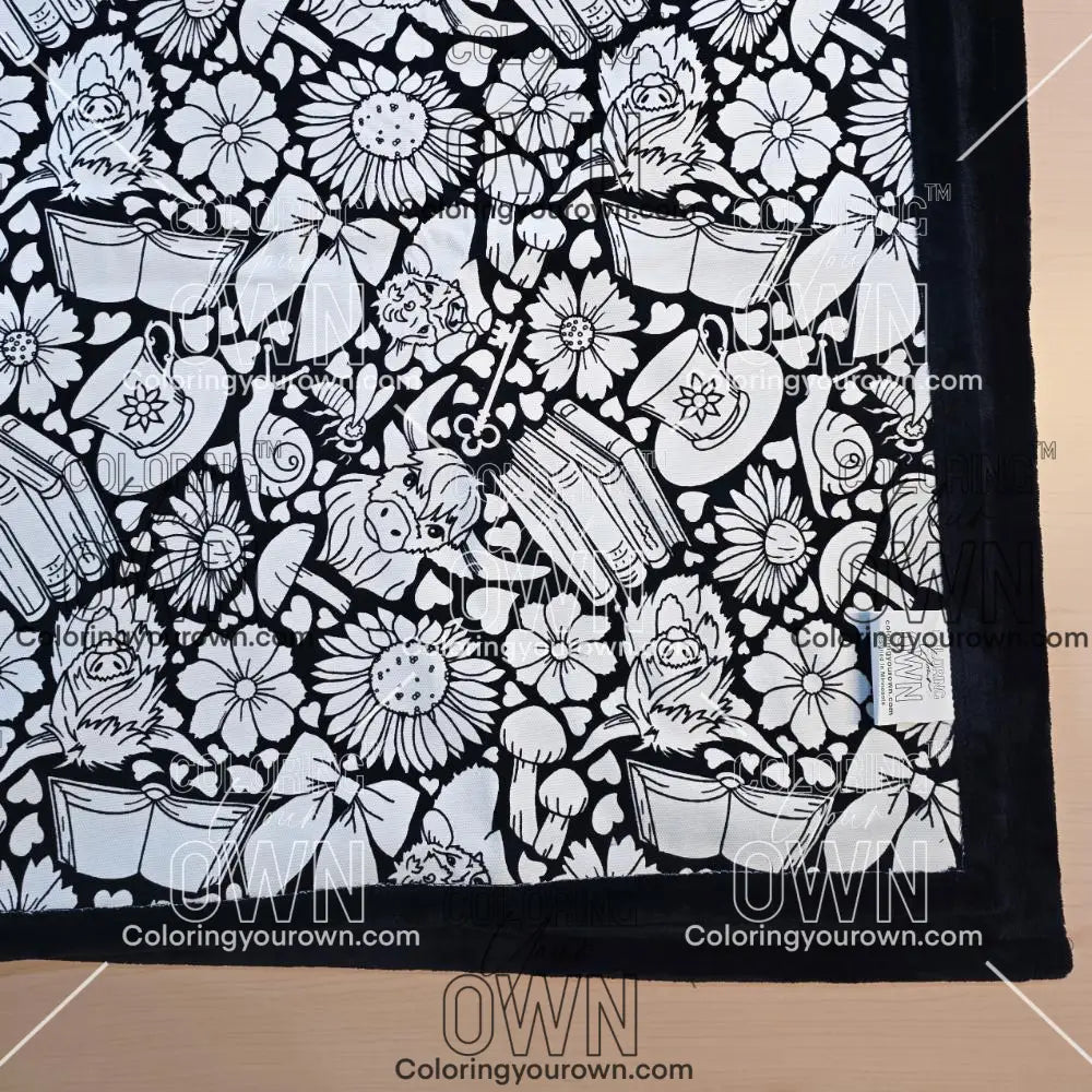 Black and white uncolored highland cow with books and tea  patterned blanket with black fleece lined underside close up view