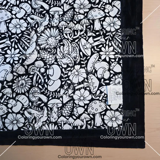 Black and white uncolored mushroom and floral patterned blanket with black fleece lined underside close up view