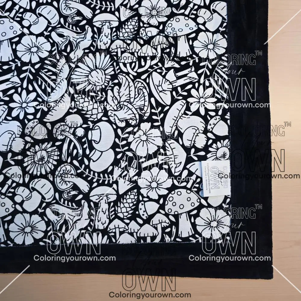 Black and white uncolored mushroom and floral patterned blanket with black fleece lined underside close up view