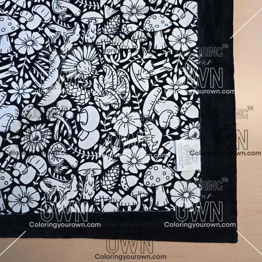 Black and white uncolored mushroom and floral patterned blanket with black fleece lined underside close up view