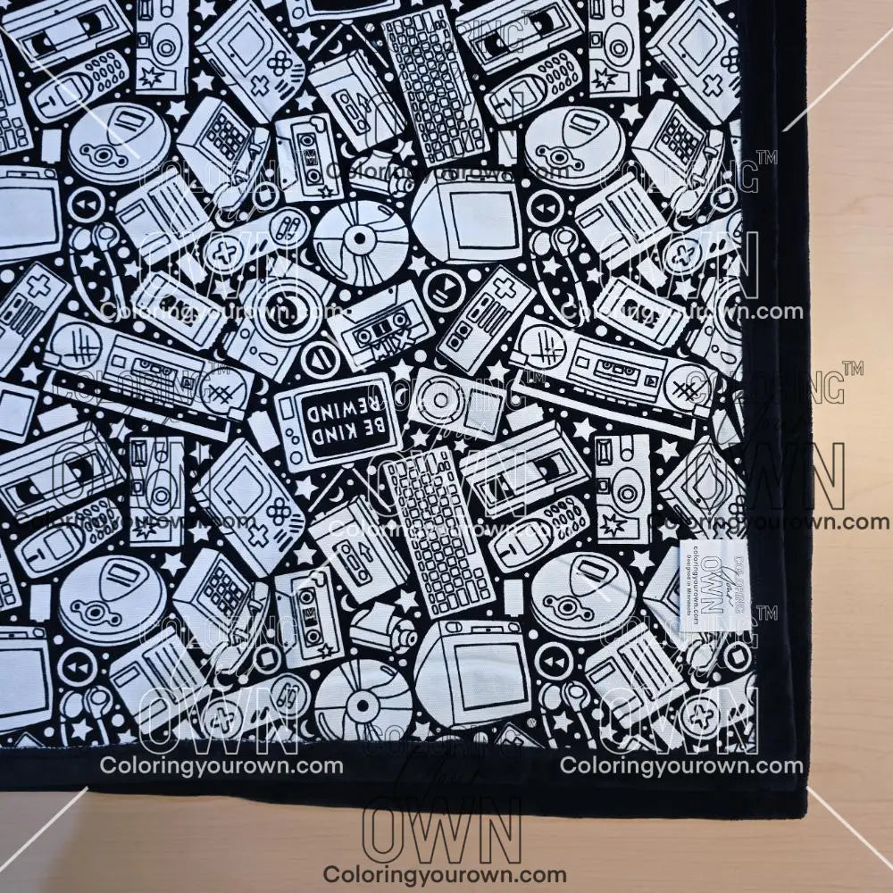 Black and white uncolored retro technology, keyboard ,camera and stereo patterned blanket with black fleece lined underside close up view