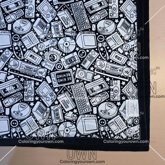 Black and white uncolored retro technology, keyboard ,camera and stereo patterned blanket with black fleece lined underside close up view