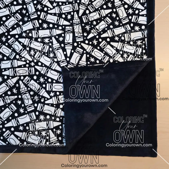 Black and white uncolored many crayon patterned blanket with close up view showing black fleece lined underside