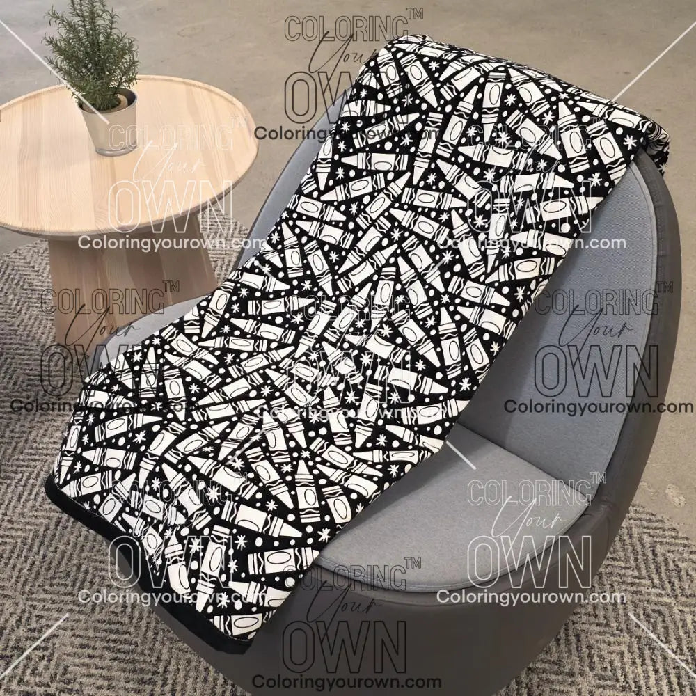 Black and white uncolored many crayon patterned blanket with a black fleece lined underside draped over a gray chair.