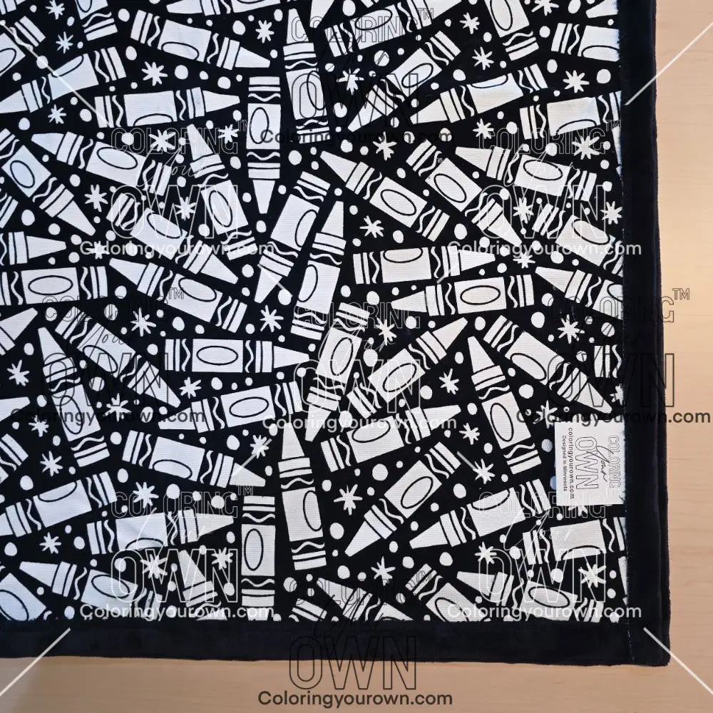 Black and white uncolored many crayon patterned blanket with black fleece lined underside close up view