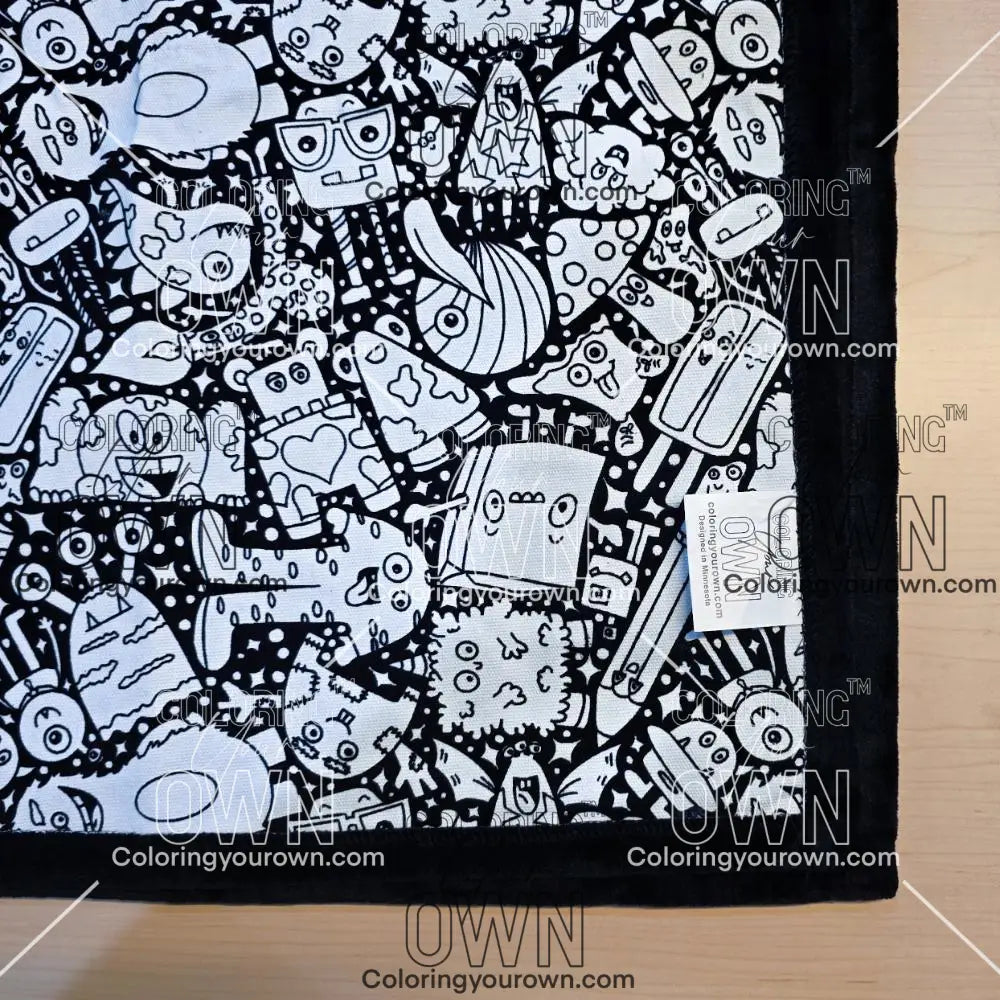 Black and white uncolored  silly monster party patterned blanket with black fleece lined underside close up view