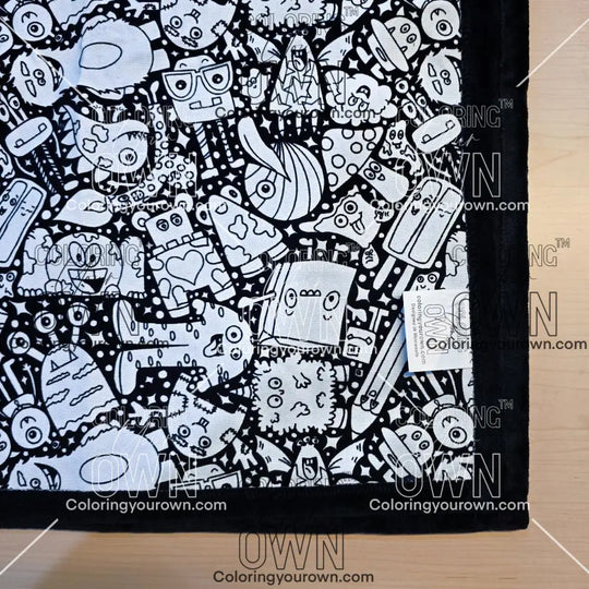 Black and white uncolored  silly monster party patterned blanket with black fleece lined underside close up view