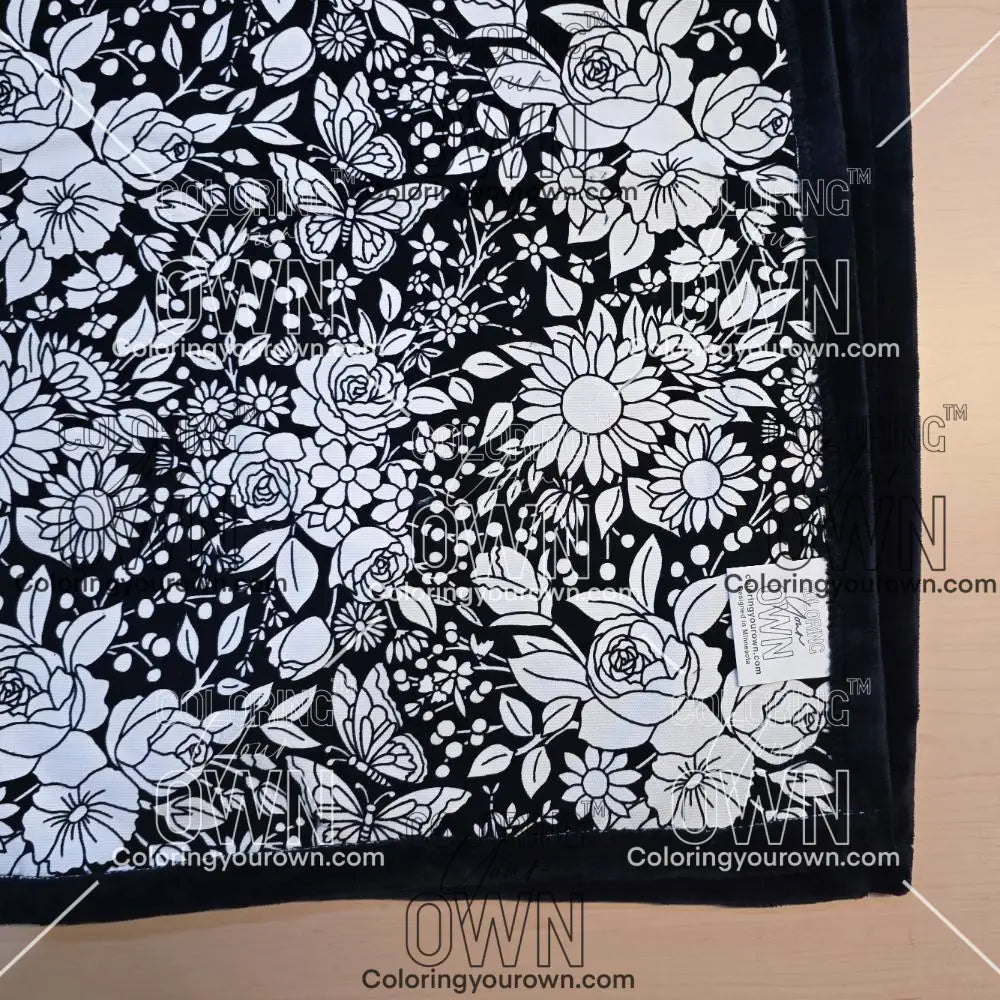 Black and white uncolored vintage floral and butterfly patterned blanket with black fleece lined underside close up view