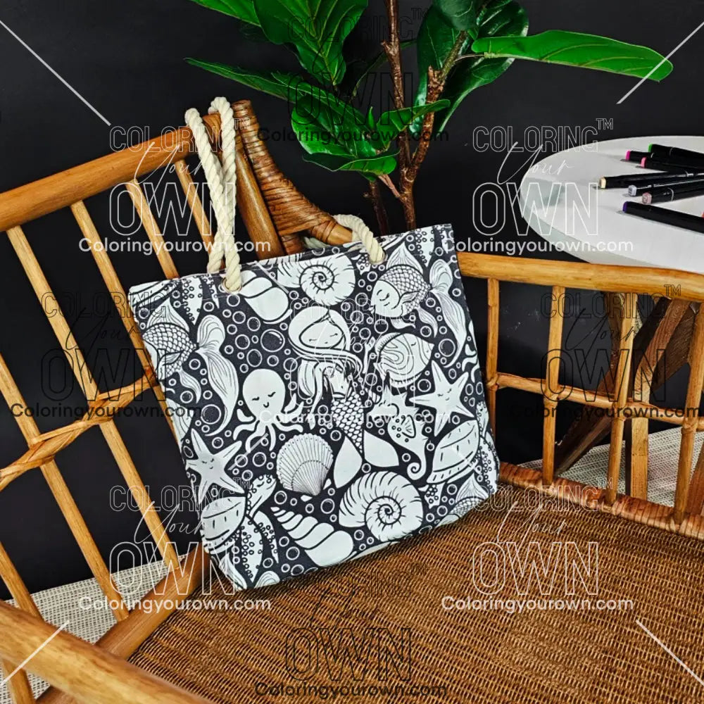 photo of an uncolored color your own tote sitting on a wicker chair beside a table with markers