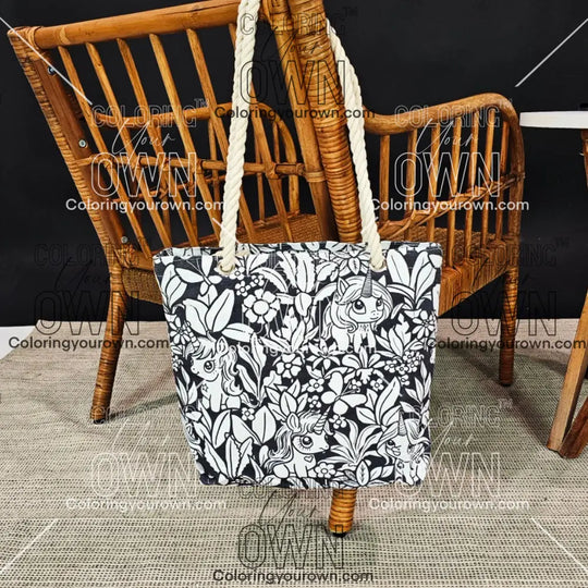 photo of a unicorn uncolored color your own tote hanging on the back of a wicker chair.