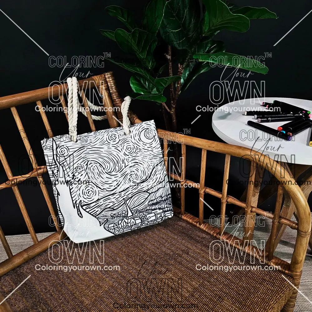 photo of an uncolored starry night color your own tote sitting on a wicker chair beside a table with markers. 