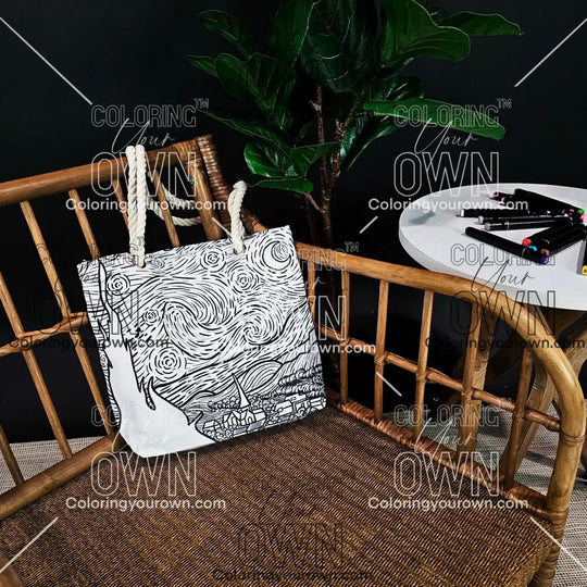 photo of an uncolored starry night color your own tote sitting on a wicker chair beside a table with markers. 