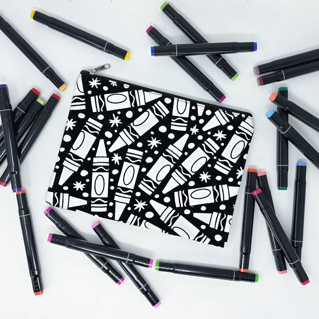 Photo of a black and white flat makeup bag with lots of colorful markers beside it indicating the customer gets to color it when they receive theirs. This is the same bag as the pencil case