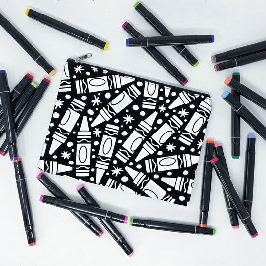 Photo of a black and white flat makeup bag with lots of colorful markers beside it indicating the customer gets to color it when they receive theirs. This is the same bag as the pencil case