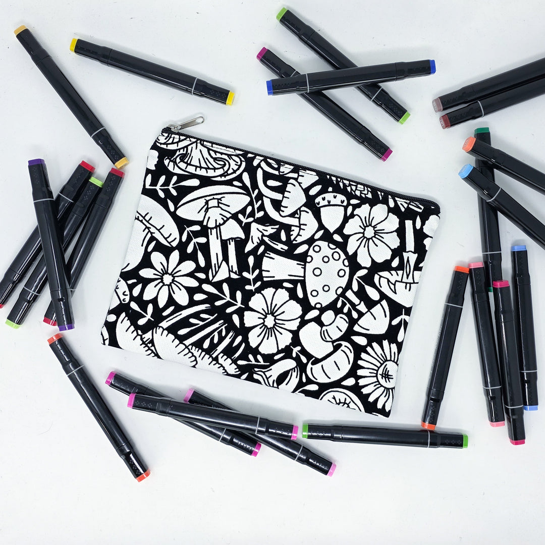 Photo of a black and white flat pencil pouch with lots of colorful markers beside it indicating the customer gets to color it when they receive theirs. This is the same bag as the pencil case and makeup bag - Side A - this bag has images of mushrooms on it