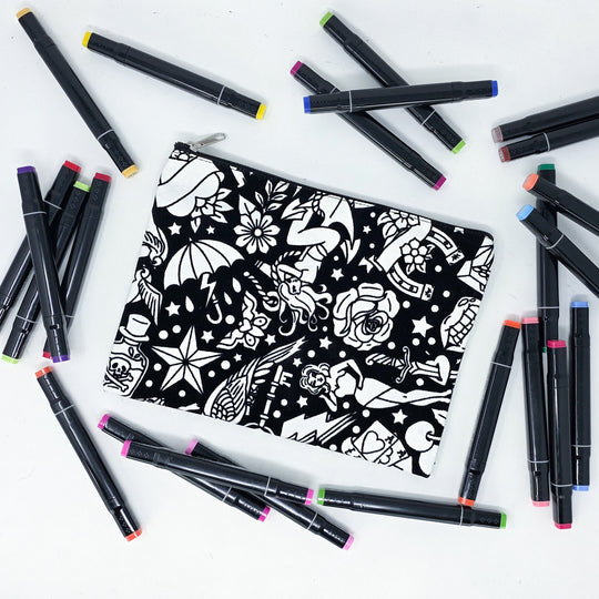 Photo of a black and white flat pencil pouch with lots of colorful markers beside it indicating the customer gets to color it when they receive theirs. This is the same bag as the pencil case and makeup bag - Side B - this bag has images of traditional tattoo-inspired graphics including pinup girls, cigarettes, roses, birds, vampire lips, cards, poison bottles, and more