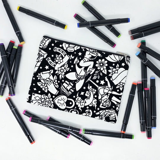 Photo of a black and white flat pencil pouch with lots of colorful markers beside it indicating the customer gets to color it when they receive theirs. This is the same bag as the pencil case and makeup bag - Side A - this bag has images of traditional tattoo-inspired graphics including pinup girls, cigarettes, roses, birds, vampire lips, cards, poison bottles, and more