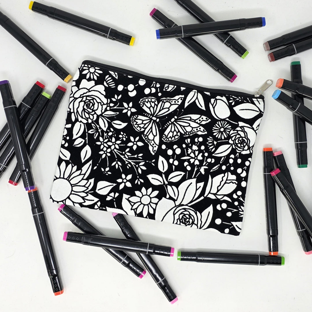 Photo of a black and white flat pencil pouch with lots of colorful markers beside it indicating the customer gets to color it when they receive theirs. This is the same bag as the pencil case - Side B - this bag has images of vintage flowers on it