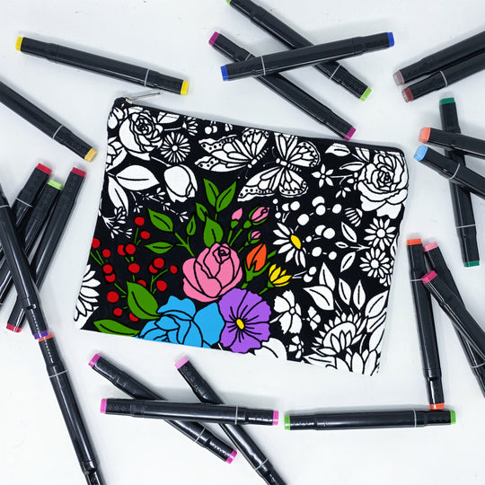 Photo of a black and white flat pencil pouch with lots of colorful markers beside it indicating the customer gets to color it when they receive theirs. This is the same bag as the pencil case - this one is partially colored - this bag has images of vintage flowers on it