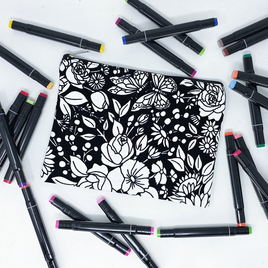 Photo of a black and white flat pencil pouch with lots of colorful markers beside it indicating the customer gets to color it when they receive theirs. This is the same bag as the pencil case - Side A - this bag has images of vintage flowers on it